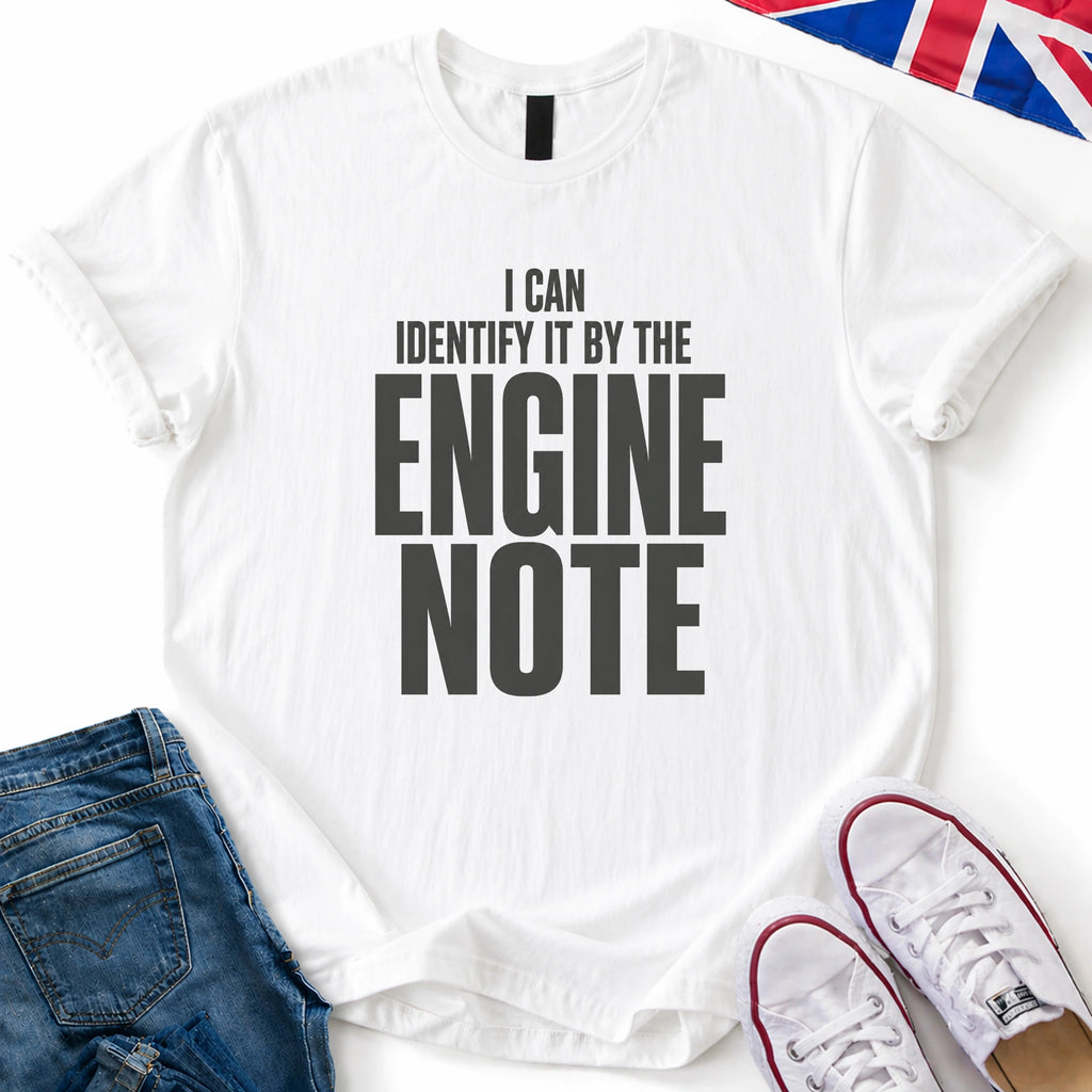 A white short-sleeve graphic T-shirt laid flat with the text 'I CAN IDENTIFY IT BY THE ENGINE NOTE' in large black letters. The shirt is styled with blue jeans, white sneakers, and a small Union Jack flag corner on a white background.